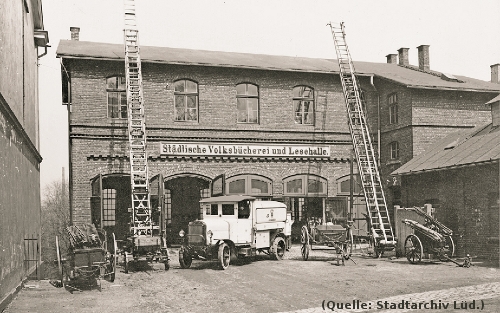 Foto: Ein Haus. Davor ein alter Feuerwehrwagen und zwei lange Leitern.Aufschrift auf dem Haus: 'Städtische Volksbücherei und Lesehalle'