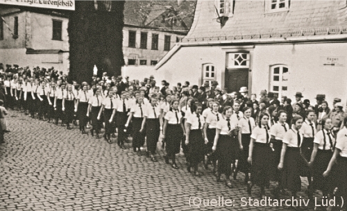 Foto: Auf einer Strasse marschieren Mädchen und junge Frauen. Im Hintergrund Häuser.